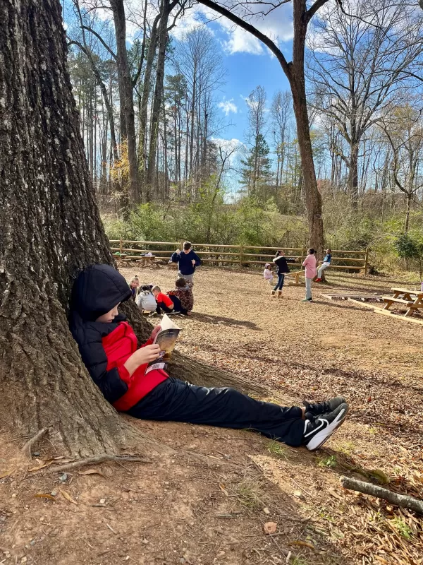 Child reading a book while leaning against a tree