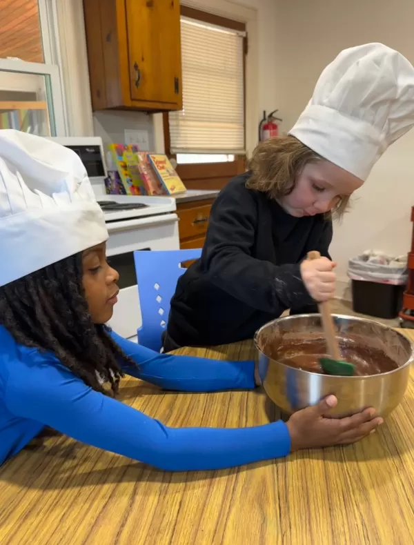 One child mixing cake mix while another child holds the bowl